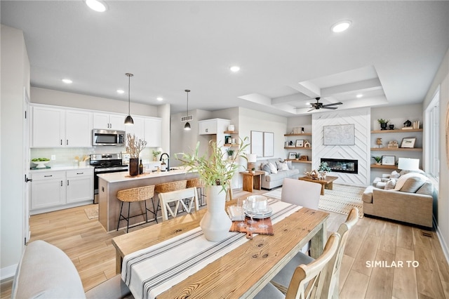 interior space with coffered ceiling, light hardwood / wood-style floors, a fireplace, ceiling fan, and sink