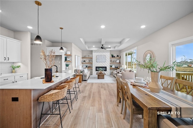 dining area with sink, ceiling fan, light hardwood / wood-style flooring, a fireplace, and a tray ceiling