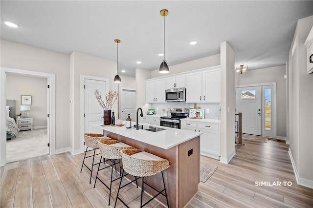 kitchen featuring decorative light fixtures, a center island with sink, light hardwood / wood-style flooring, a breakfast bar area, and appliances with stainless steel finishes