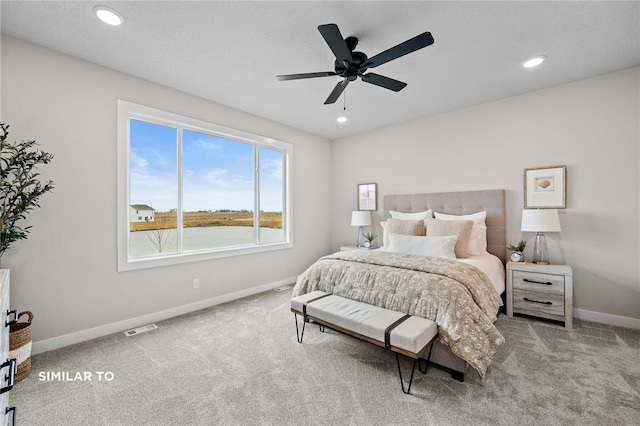 bedroom with light colored carpet, ceiling fan, and a water view