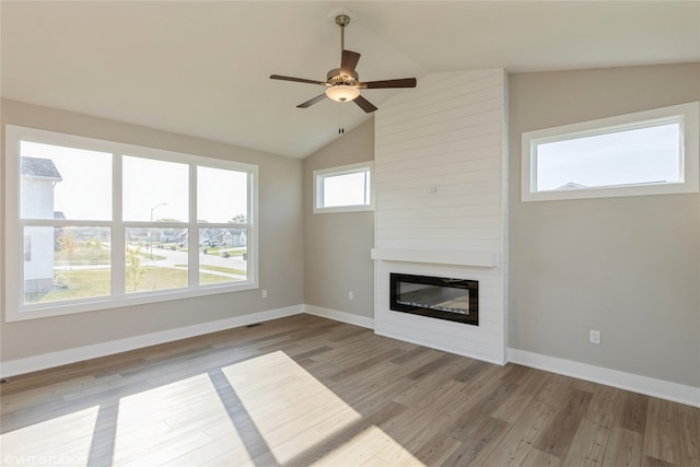 unfurnished living room featuring light wood-type flooring, lofted ceiling, ceiling fan, and a large fireplace