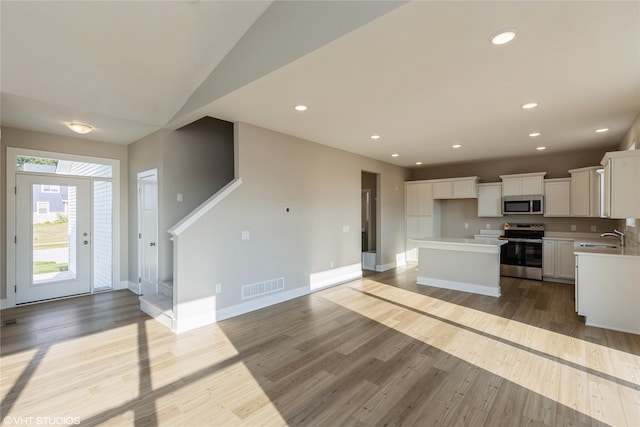 kitchen with a kitchen island, stainless steel appliances, sink, white cabinetry, and light wood-type flooring