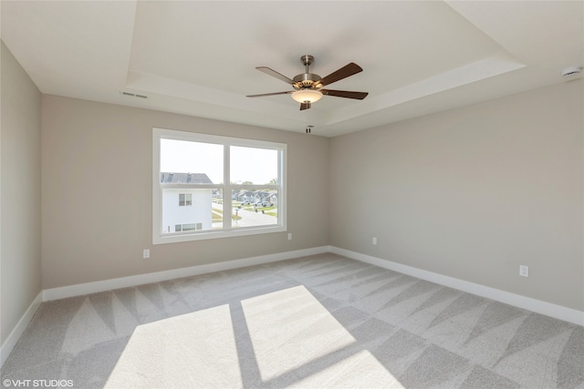 carpeted empty room with a raised ceiling and ceiling fan