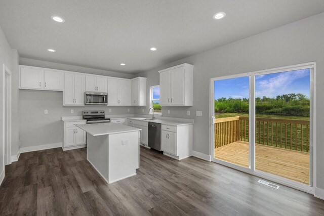 kitchen with appliances with stainless steel finishes, a wealth of natural light, white cabinets, dark hardwood / wood-style floors, and a kitchen island