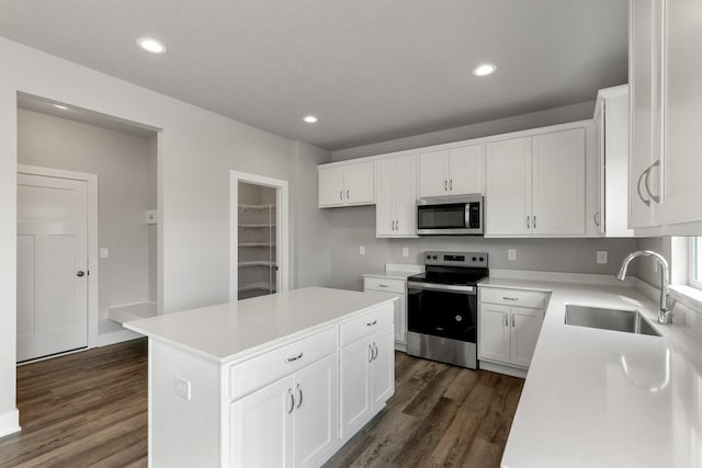 kitchen with dark wood-type flooring, white cabinets, sink, appliances with stainless steel finishes, and a kitchen island