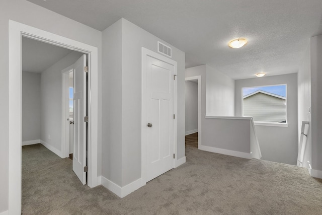 corridor featuring light carpet and a textured ceiling