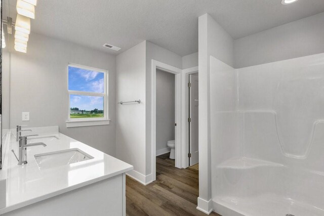 bathroom featuring vanity, a shower, hardwood / wood-style flooring, toilet, and a textured ceiling