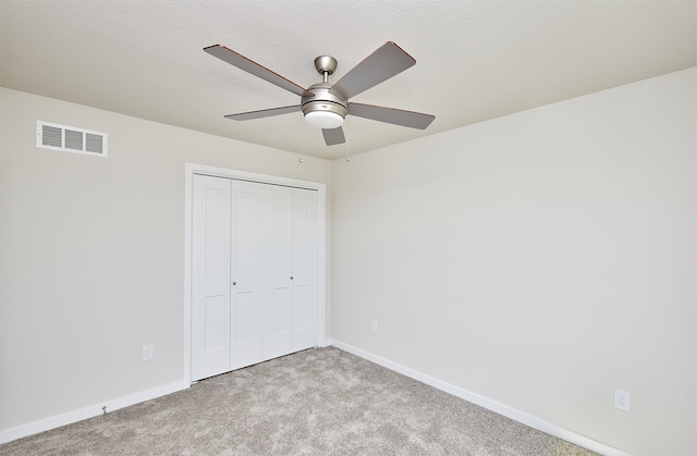 unfurnished bedroom featuring a closet, ceiling fan, light colored carpet, and a textured ceiling