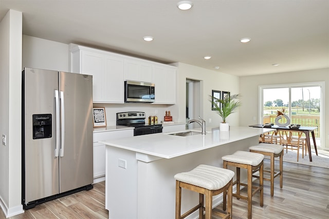 kitchen featuring light wood-type flooring, appliances with stainless steel finishes, white cabinets, and a kitchen island with sink