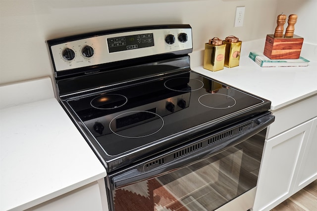 details featuring stainless steel electric range oven, white cabinets, and light hardwood / wood-style flooring