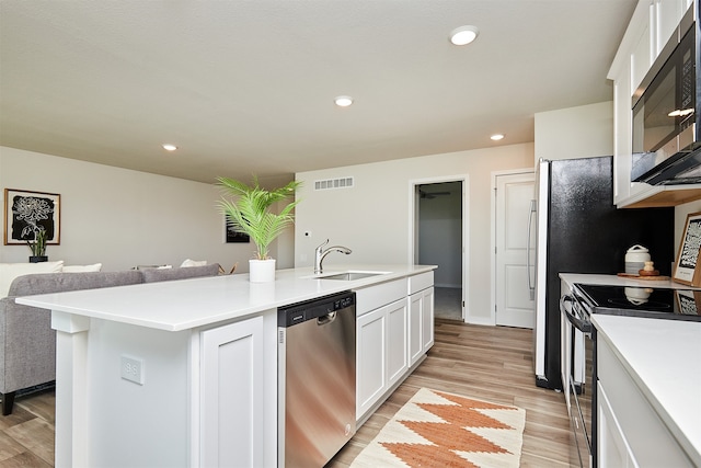 kitchen featuring light wood-type flooring, white cabinetry, sink, appliances with stainless steel finishes, and a center island with sink