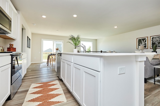 kitchen with a kitchen island with sink, appliances with stainless steel finishes, white cabinetry, and light hardwood / wood-style flooring