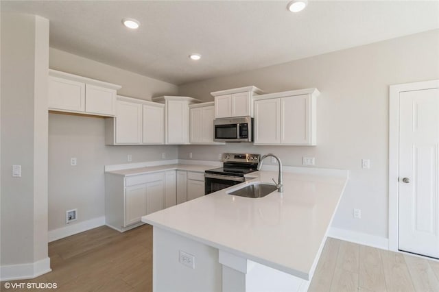 kitchen featuring kitchen peninsula, stainless steel appliances, sink, light hardwood / wood-style flooring, and white cabinets