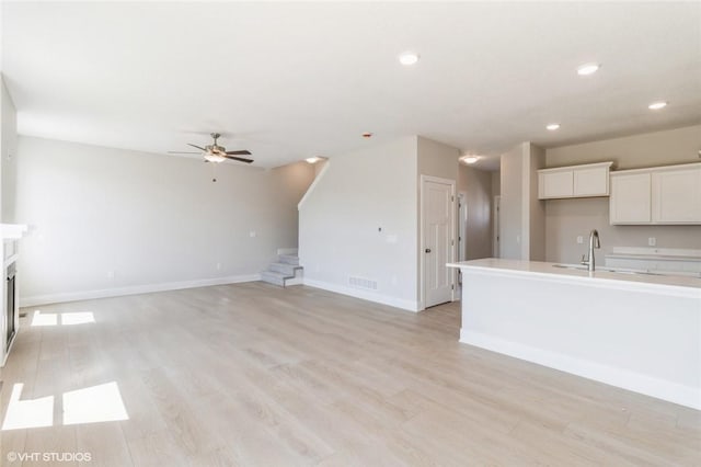 unfurnished living room with a premium fireplace, light hardwood / wood-style floors, ceiling fan, and sink