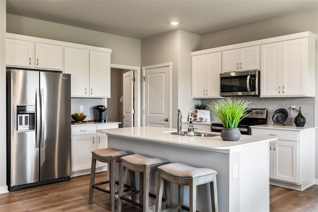 kitchen with dark wood-type flooring, a center island with sink, a sink, white cabinetry, and stainless steel appliances