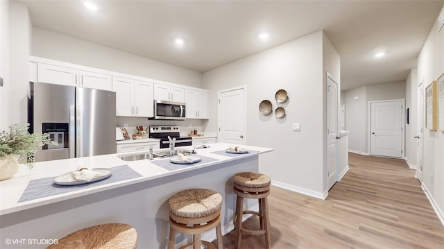 kitchen with sink, light hardwood / wood-style flooring, a breakfast bar, white cabinetry, and stainless steel appliances