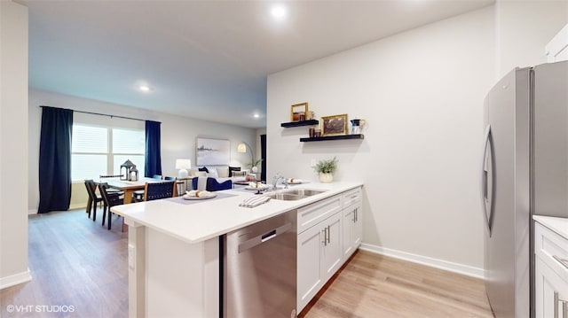 kitchen featuring sink, light wood-type flooring, kitchen peninsula, stainless steel appliances, and white cabinets