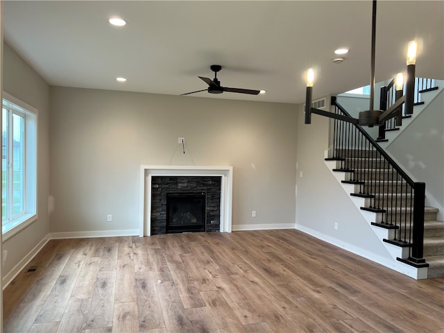 unfurnished living room with ceiling fan, wood-type flooring, and a stone fireplace