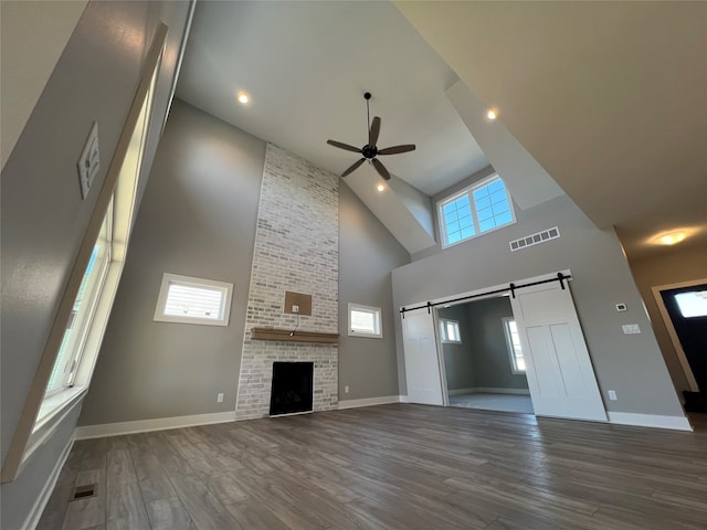 unfurnished living room featuring ceiling fan, high vaulted ceiling, a fireplace, a barn door, and dark hardwood / wood-style flooring