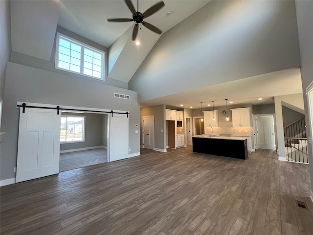 unfurnished living room with a barn door, dark hardwood / wood-style floors, sink, and high vaulted ceiling