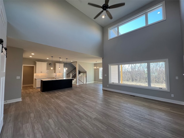 unfurnished living room with a high ceiling, sink, ceiling fan with notable chandelier, a barn door, and dark wood-type flooring