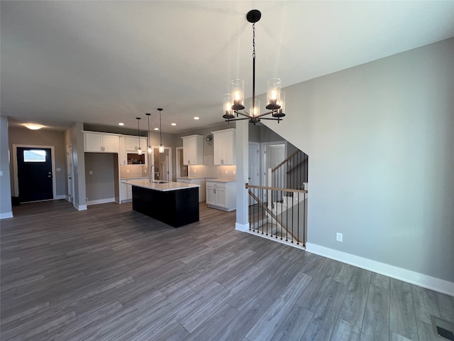 kitchen with white cabinetry, a center island with sink, decorative light fixtures, a notable chandelier, and dark hardwood / wood-style flooring