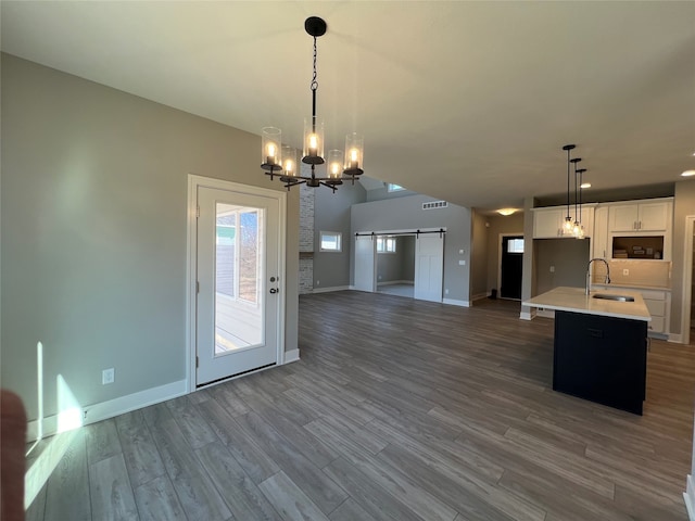 kitchen with sink, an island with sink, white cabinets, a barn door, and pendant lighting