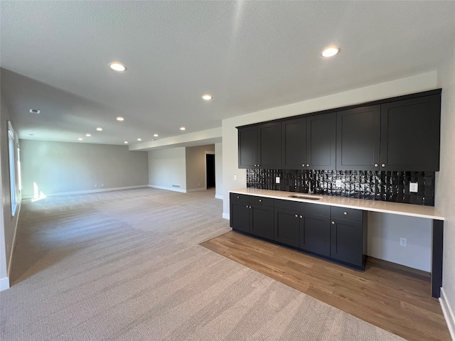 kitchen featuring a textured ceiling, decorative backsplash, light carpet, and sink