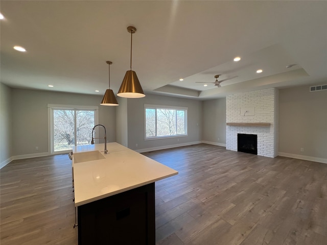 kitchen with wood-type flooring, pendant lighting, sink, an island with sink, and a brick fireplace