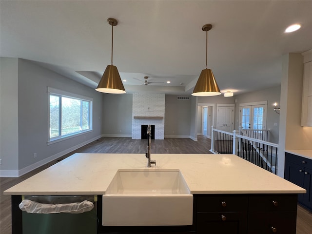 kitchen featuring sink, stainless steel dishwasher, a fireplace, a kitchen island, and dark hardwood / wood-style flooring