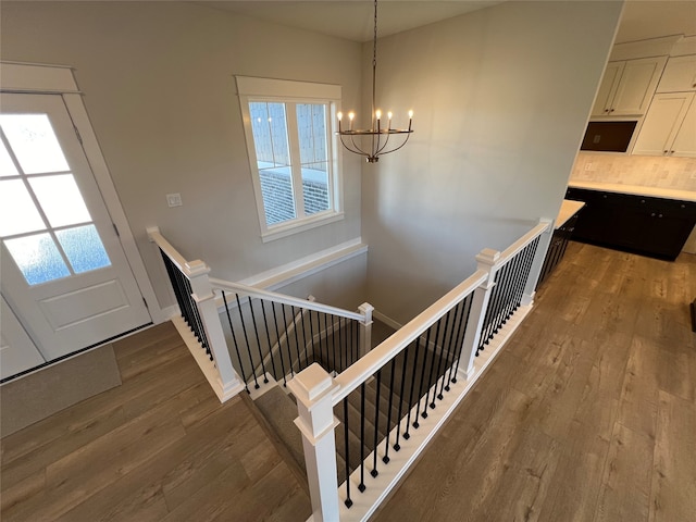 stairway featuring a wealth of natural light, wood-type flooring, and a notable chandelier