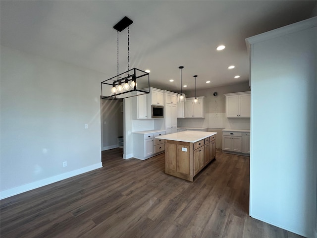 kitchen with dark wood-type flooring, stainless steel microwave, a kitchen island, white cabinetry, and decorative light fixtures