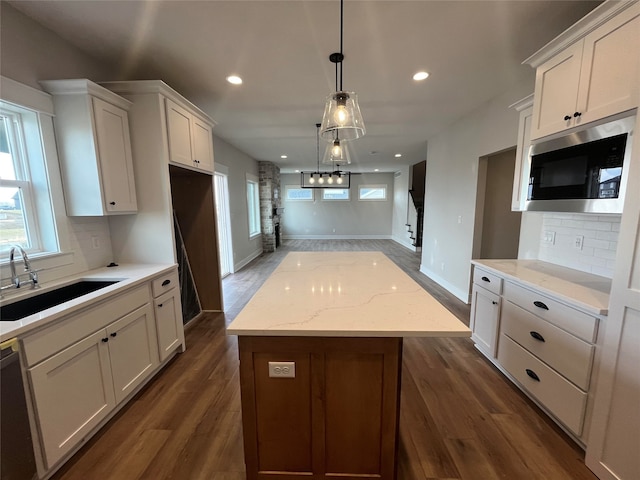 kitchen featuring dark hardwood / wood-style floors, a kitchen island, stainless steel microwave, white cabinets, and pendant lighting