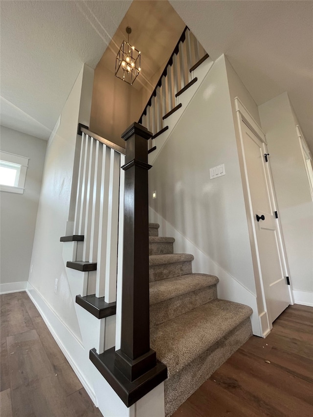 staircase with hardwood / wood-style flooring, a textured ceiling, and an inviting chandelier