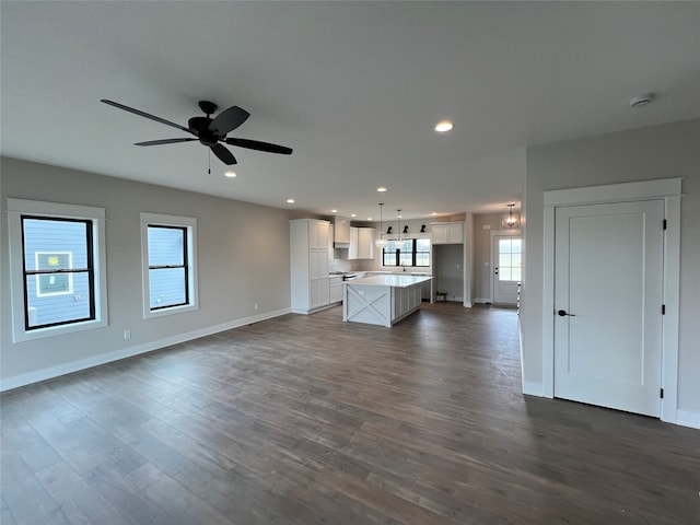 unfurnished living room with plenty of natural light, dark wood-type flooring, and ceiling fan