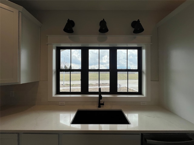 kitchen with tasteful backsplash, white cabinets, light stone countertops, sink, and dishwashing machine