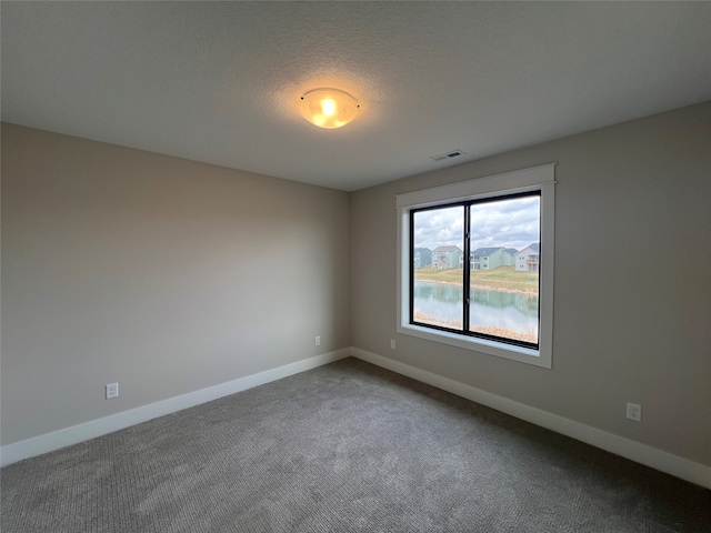 carpeted empty room with a water view and a textured ceiling