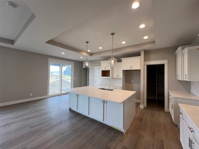 kitchen featuring white cabinets, hanging light fixtures, a kitchen island with sink, dark hardwood / wood-style floors, and a raised ceiling