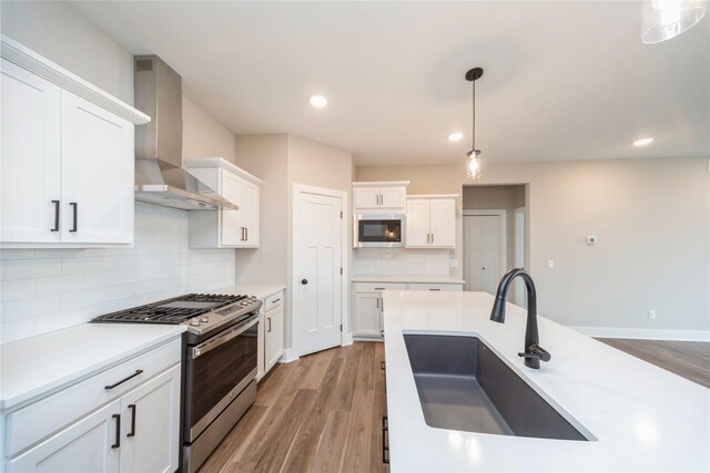 kitchen featuring white cabinetry, wall chimney range hood, stainless steel appliances, sink, and hanging light fixtures