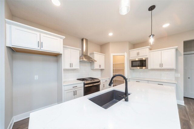 kitchen with appliances with stainless steel finishes, wall chimney exhaust hood, decorative light fixtures, white cabinetry, and sink