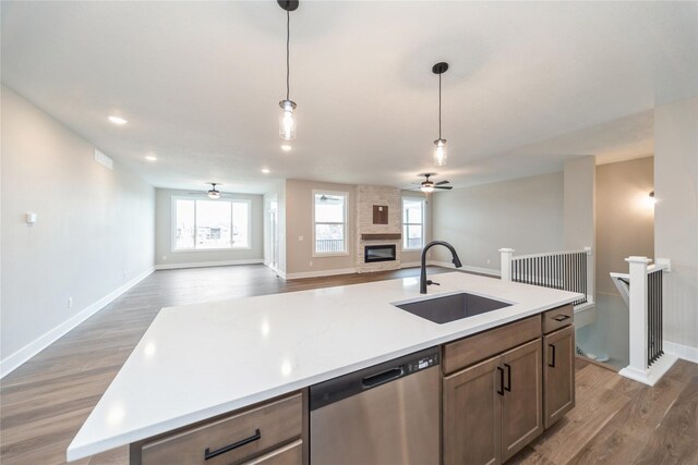 kitchen featuring a kitchen island with sink, stainless steel dishwasher, sink, decorative light fixtures, and a large fireplace