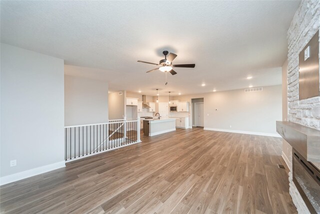 unfurnished living room with sink, ceiling fan, a stone fireplace, and hardwood / wood-style floors