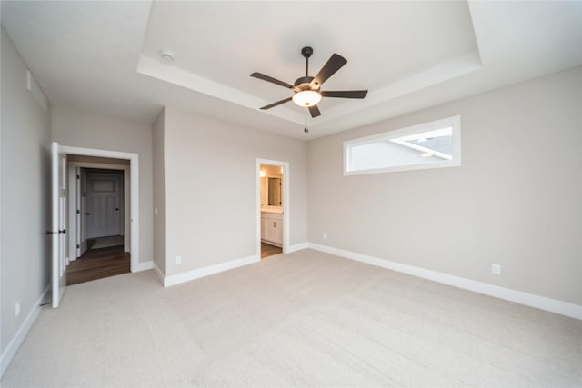 unfurnished bedroom with ceiling fan, ensuite bathroom, a raised ceiling, and light colored carpet