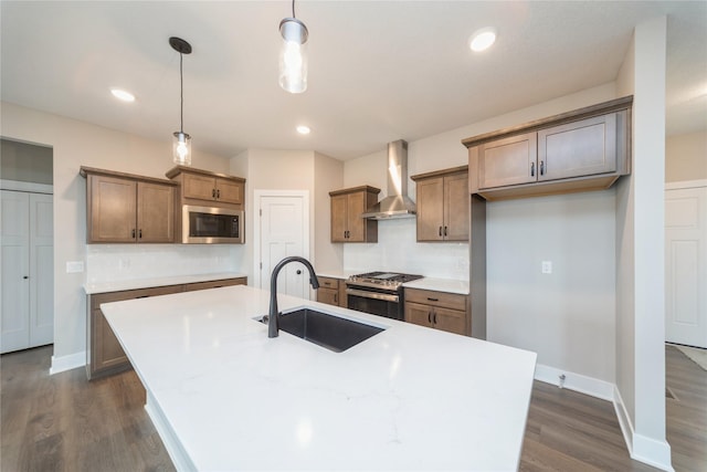 kitchen with gas range, sink, wall chimney range hood, and a kitchen island with sink