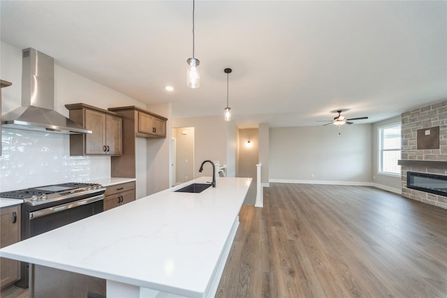 kitchen featuring wall chimney exhaust hood, sink, decorative light fixtures, a kitchen island with sink, and decorative backsplash