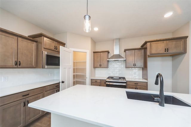 kitchen featuring wall chimney exhaust hood, decorative light fixtures, stainless steel gas stove, sink, and built in microwave