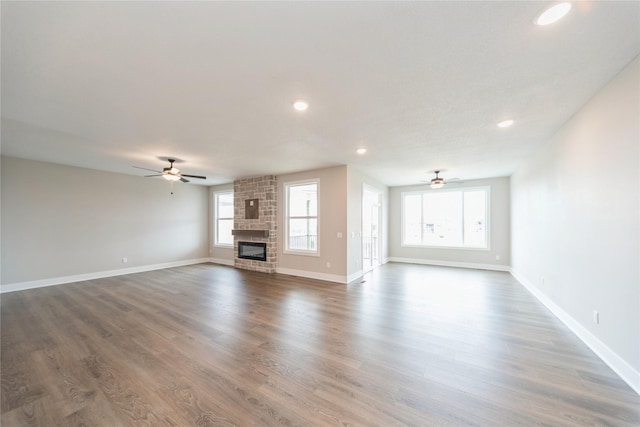 unfurnished living room with ceiling fan, a stone fireplace, and hardwood / wood-style floors