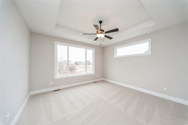 carpeted spare room with ceiling fan and a raised ceiling