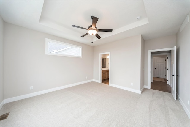 unfurnished bedroom featuring light colored carpet, ensuite bathroom, ceiling fan, and a raised ceiling