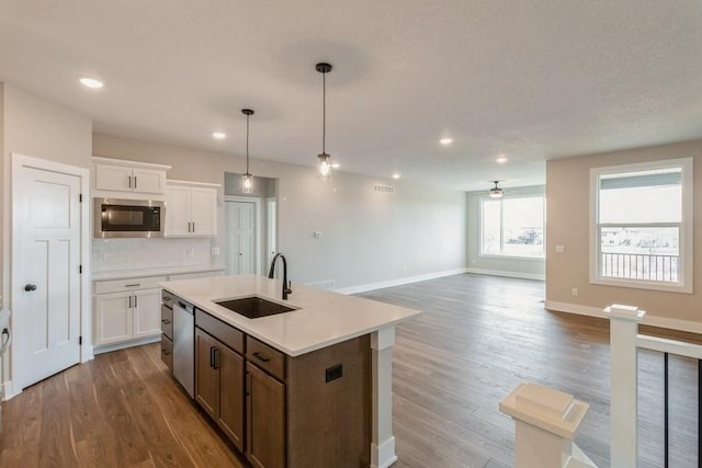 kitchen featuring sink, hanging light fixtures, stainless steel appliances, a center island with sink, and white cabinets